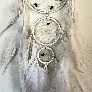 May include: White dream catcher with three hoops and white feathers. The hoops are decorated with black beads.