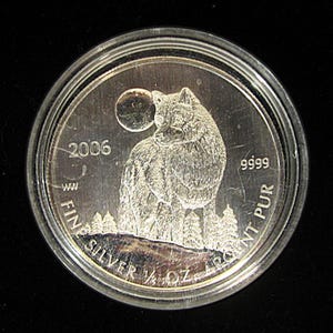May include: A silver coin with a wolf design. The coin is dated 2006 and reads "Fine Silver 1/4 oz 9999 Argent Pur".