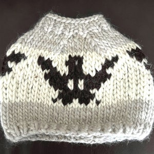 May include: A hand-knitted, gray, white, and black hat with a unique geometric pattern. The hat is designed to be worn with a ponytail or bun. The color scheme includes shades of gray, off-white, and black, creating a cozy and stylish accessory.