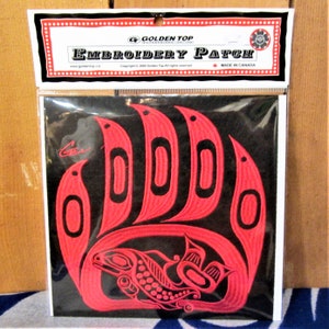 Può includere: Toppa ricamata rossa di una zampa d'orso con un salmone all'interno. La toppa è su uno sfondo nero e ha il testo "Golden Top" e "Embroidery Patch" sulla confezione.
