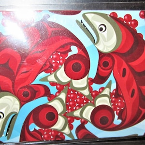 May include: A vibrant, stylized illustration featuring salmon in shades of red and maroon against a light blue background. The design incorporates circular and curved shapes, with the artist's signature in the lower left corner. The artwork evokes a sense of movement and cultural artistry.