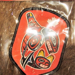 May include: A red, black and white embroidered patch featuring a stylised image of a bird and a fish. The patch is bordered in black and has a small Canadian flag in the top right corner.