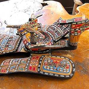 May include: A detailed wooden sculpture, hand-carved with a bird design. The artwork features red, blue, and yellow accents. The sculpture is displayed on a wooden surface. The measurements are in centimetres.