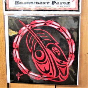 Può includere: Toppa ricamata rossa e bianca con un'immagine stilizzata di un pesce circondato da un cerchio di piume. La toppa è su uno sfondo nero. Il testo "EMBROIDERY PATCH" è in cima alla toppa. Il testo "MADE IN CANADA" è in fondo alla toppa.