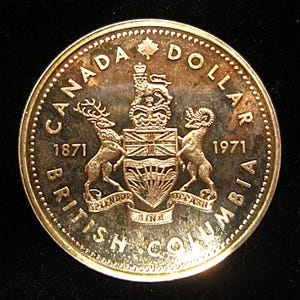 May include: Gold-coloured Canadian dollar coin commemorating the 100th anniversary of British Columbia. The coin features the Canadian coat of arms with the years 1871 and 1971.