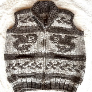 May include: A gray and white knitted vest with a zipper closure and a geometric pattern. The vest has a high collar and no sleeves.