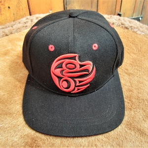 May include: Black and red baseball cap with a red embroidered design of a stylized bird on the front.