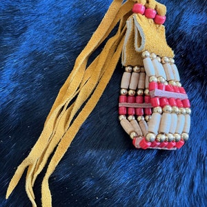 May include: A beaded leather tassel with red and gold beads, and a long fringe of yellow leather.