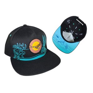 Può includere: Cappellino nero a tesa piatta con una toppa circolare raffigurante un'aquila in volo, un sole e un paesaggio montano. Il cappellino presenta un design turchese e bianco con un alce e alberi. L'interno della visiera è azzurro con un motivo di tartarughe e pesci.