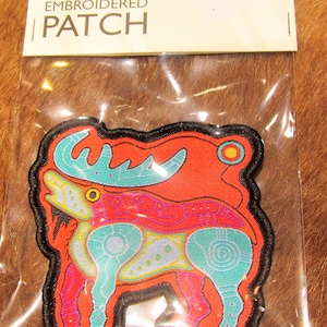 Può includere: Toppa ricamata da stirare con un designo stilizzato di alce colorato. L'alce è contornato di nero e ha un corpo rosso con dettagli blu, verdi, gialli e viola. La toppa è etichettata "iron-on embroidered patch".