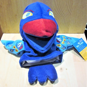 May include: A blue plush puppet shaped like a bird with a red beak and yellow eyes. The puppet has blue wings with embroidered details. The puppet has the text "Tricky the Raven" on a tag.