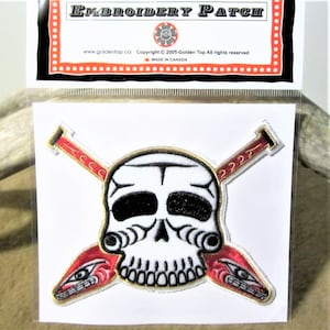 Può includere: Toppa ricamata con un teschio bianco con bordi dorati e pagaie rosse incrociate con bordi dorati. Le pagaie hanno occhi stilizzati e il testo "2222" e "ACCO" è ricamato sulle pagaie. Il testo "EMBROIDERY PATCH" è stampato sulla confezione.