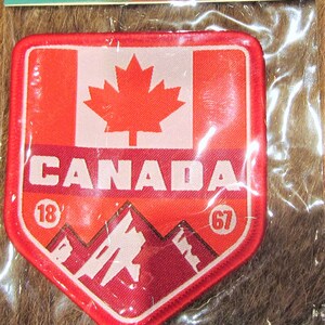 May include: Red, white and red Canadian flag patch with the word "CANADA" in white letters. The patch also features a white mountain range and the numbers "18" and "67" in gold circles.