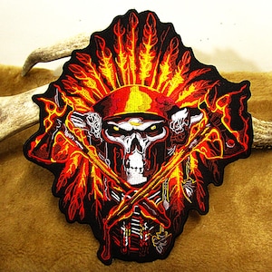 May include: A black embroidered patch featuring a skull wearing a red and yellow headdress with flames. The skull is holding two crossed tomahawks with flames.