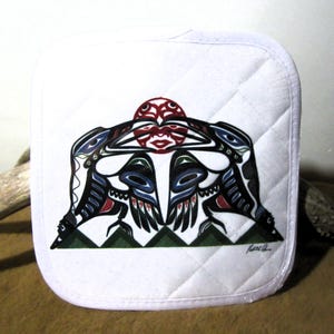 May include: White quilted pot holder featuring a colourful design of two stylised birds facing each other with a red circle in the centre. The design is in the style of Northwest Coast Indigenous art. The artist's signature is in the bottom right corner.