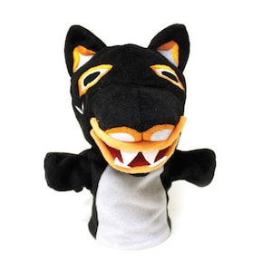 May include: Black and orange plush puppet with a toothy grin. The puppet is shaped like a wolf or dog with a white belly.
