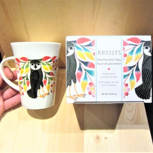 May include: White ceramic mug with a black and white owl illustration and colorful floral design. The mug is in a box with the text "ARTISTS Fine Porcelain Mug Tasse de porcelaine" and information about the origin of the design.