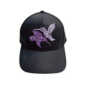 May include: Black baseball cap with embroidered purple hummingbirds. The cap has a curved peak and a button on top. The hummingbird design features detailed patterns, creating a striking contrast against the dark fabric.