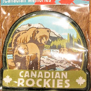 May include: A green and brown embroidered patch featuring a scene of two brown bears in front of a mountain range. The text "CANADIAN ROCKIES" is on the bottom of the patch with a maple leaf on each side.