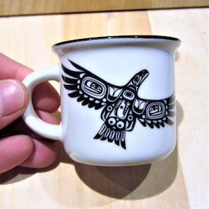 May include: White ceramic mug with a black and white stylized image of a bird with outstretched wings. The bird is in a traditional Native American design.
