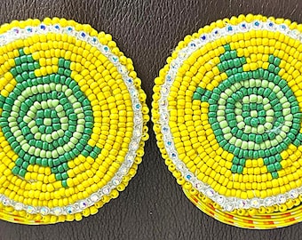 May include: Two round beaded ornaments with a green turtle design on a yellow background. The turtles are surrounded by a white beaded border.