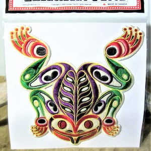May include: Embroidered patch of a frog with green, purple, white, red, and yellow details. The patch is made in Canada and has the text "Embroidery Patch" on the top.