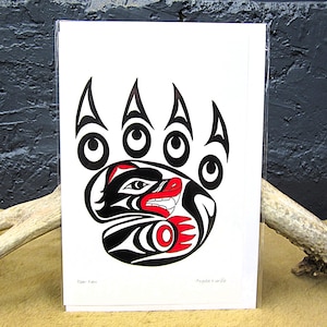May include: A white card featuring a black and red bear paw design in a Native American style. The bear paw has five claws and a detailed design within the paw. The card is in a clear plastic sleeve.