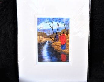 May include: Framed print of a painting depicting three figures in traditional clothing walking along a path by a stream in a forest setting. The figures are wearing red, purple, and blue clothing. The stream is surrounded by trees and bushes. The sky is blue with white clouds.