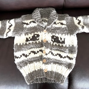 May include: A gray and white knitted cardigan with a button-up front and a collar. The cardigan has a geometric pattern.
