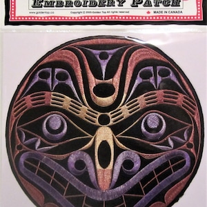 May include: Embroidered patch featuring a colourful, stylised face design. The face is black with red, purple and gold accents. The patch is round and has a black border.