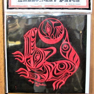 Peut inclure: Un écusson brodé rouge sur fond noir représentant un motif stylisé d'une créature avec une forme circulaire au-dessus. Le motif est dans le style de l'art autochtone de la côte nord-ouest. L'écusson est étiqueté "Embroidery Patch" et "Made in Canada".