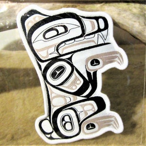 May include: A white fabric patch with a black and grey stylised design of a wolf or dog. The design is in the style of Northwest Coast Indigenous art.