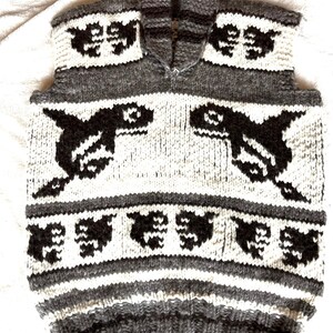 May include: A sleeveless knitted vest with a hood, featuring a white and gray color scheme. The vest has a pattern of black orcas and other geometric shapes.
