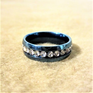 Peut inclure: Une bague bleue ornée d'une rangée de pierres scintillantes et transparentes. La bague a une finition lisse et polie et un design moderne. C'est un bijou.