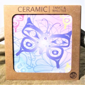 Könnte beinhalten: Keramische Untersetzer und Wandfliese mit einem blauen Schmetterling auf einem rosa, blauen und gelben Blumenhintergrund. Der Text "CERAMIC | TRIVET & WALL TILE" ist auf der Verpackung aufgedruckt.