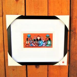 May include: Framed print of a colourful painting depicting a group of people sitting in a circle. The people are all wearing different colours and have long black hair. The background is a bright orange with a sunset scene.