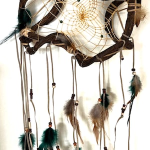 May include: A dreamcatcher with a brown wooden frame and a white web. The dreamcatcher has green and brown feathers hanging from it.
