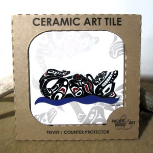 May include: A white ceramic art tile with a black and red design of a wolf and a wolf pup. The tile is framed in a cardboard box with the text "Ceramic Art Tile" and "Trivet/Counter Protector".