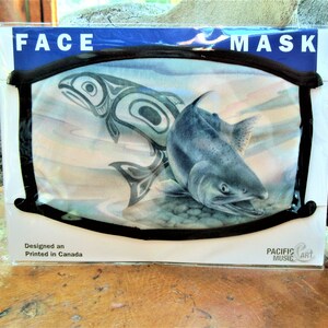 May include: A face mask with a black elastic band and a white background featuring a watercolor painting of a salmon and a stylized orca. The text "FACE MASK" is printed in blue at the top of the packaging and "Designed and Printed in Canada" is printed at the bottom. The text "PACIFIC MUSIC ART" is printed in the bottom right corner.