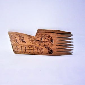 May include: A wooden comb with a carved wolf design. The comb is brown and has a natural wood finish. The wolf's face is carved in detail, with a large eye and a wide mouth.