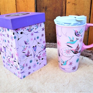 May include: A purple and pink travel mug with a lid and a matching gift box. The mug and box feature a design of stylized birds and flowers.