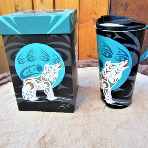 May include: A teal blue and black travel mug with a wolf howling at the moon design. The mug comes in a matching gift box with the same design.