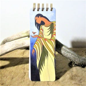 May include: A spiral bound notebook featuring a colourful illustration of a woman in a long, striped dress extending her hand towards a butterfly. The background is a blue and purple watercolour wash.