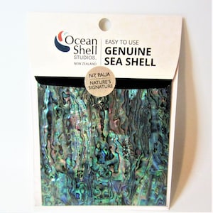 May include: A package containing a sheet of genuine New Zealand Paua shell. The shell is iridescent with shades of blue, green, and purple. The package is labelled "Ocean Shell Studios. New Zealand" and "NZ Paua Nature's Signature".