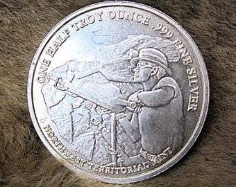 May include: A silver coin with the text "ONE HALF TROY OUNCE .999 FINE SILVER" and "Northwest Territorial Mint". The coin features a relief of a person operating machinery.