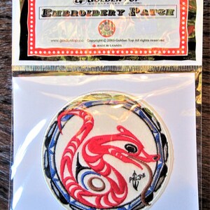 May include: A round embroidered patch with a red and white stylized design of a creature with a long tail and a small head. The creature is surrounded by a blue and white circle with a black border. The text "PALJOE" is embroidered in black in the lower right corner of the patch.