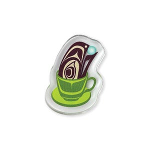 May include: A clear acrylic pin featuring a green teacup and saucer. The teacup holds a stylized design in brown and cream, with a light blue orb above. The pin has a white outline.