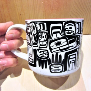 Peut inclure: Une tasse en céramique blanche avec un motif noir et blanc de figures stylisées. La tasse a une bordure rouge.