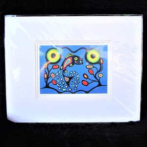 May include: A framed art print featuring a stylized fish in vibrant colors against a blue background. The fish is black with rainbow accents, surrounded by abstract shapes and plants. The artwork is encased in a white mat and a black frame.