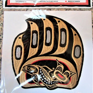 Può includere: Toppa ricamata con l'impronta di una zampa di orso nero con un salmone stilizzato al suo interno. L'impronta della zampa è bordata d'oro e il salmone di rosso. La toppa è realizzata in Canada.